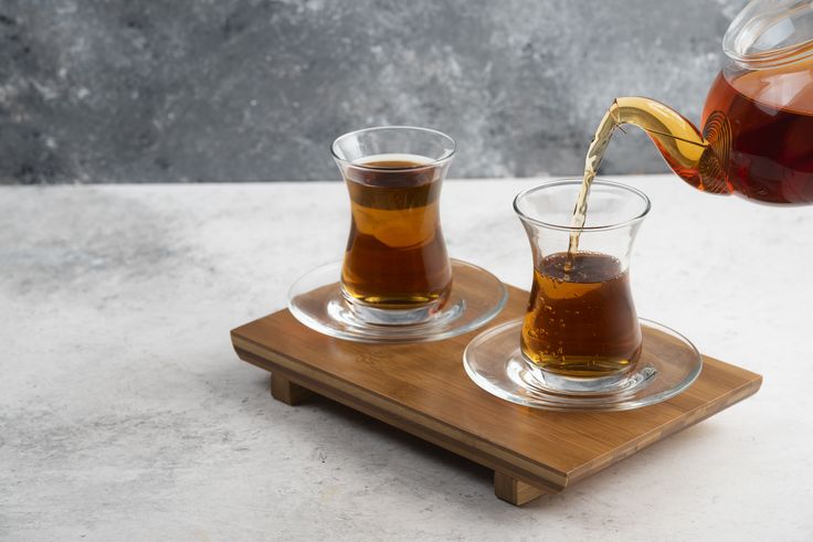 Two glass cups of tea with teapot on a wooden board